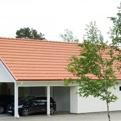 Ett vitt hus med tegeltak, där en del är en carport med två bilar och en annan del är ett garage. Kanske en ombyggnad för att bygga om carport till garage.