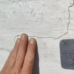 En hand pekar på en spricka i en vit tegelfasad.
