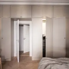 En elegant garderob i sekelskiftesstil med ljusa fronter och dörrar som leder till en walk-in closet.