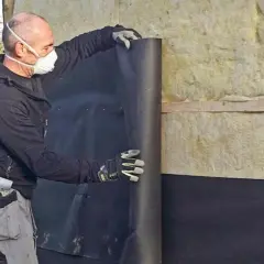 Man med mask rullar ut vindpapp på insidan av en isolerad vägg.