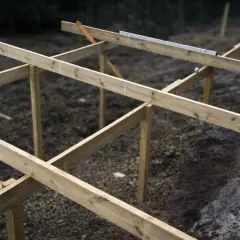 Grundarbete för altan. Träreglar och stolpar bildar stommen, redo för altan plintar eller plattor. Vattenpasset visar att allt är rakt.
