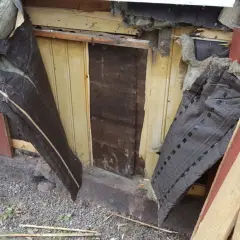 Rivning av gammalt tak. Synlig isolering och trasig vindpapp. Bräder och spillved ligger staplade.