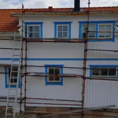 Ställningar runt ett vitt hus med orange tak. Arbetet med att isolera gammalt hus utifrån pågår.