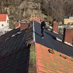 Takläggare arbetar på ett tak där gamla tegelpannor byts ut mot nytt material. Kanske funderar de på aluzink nackdelar inför framtida projekt.