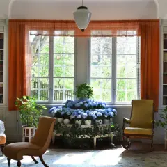 Ett rum med bokhyllor, en rund dukförsedd bord, stolar och en blomsteruppsättning. Ellen Keys inredning präglas av ljus och natur.