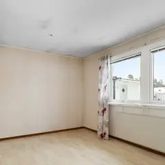 Ett rum med ljusa väggar och trägolv. Svart sot i taket syns ovanför dörren och längs kanterna. Fönster med blommig gardin och utsikt över snöklädda hus.