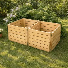 Två sektioner av en nybyggd kompostbehållare i trä står på en gräsmatta. Bredvid står en vattenkanna och krukor med blommor, redo att börja bygga kompost.