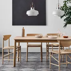 Ett ljust träbord med stolar i naturmaterial, en vas och tallrikar. Lamporna ovanför och den stora gröna växten bidrar till en känsla av antroposofisk inredning.