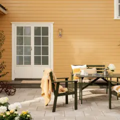 En uteplats med gröna möbler och en gul fasad ger inspiration till ett gult tegelhus. Blommor och en filt skapar en mysig känsla.