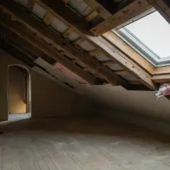 Pågår renovera vind. Synliga takbjälkar, isolering och ett takfönster. Golvet är av trä.