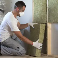 Man med skyddsutrustning installerar tjock isolering i taket.