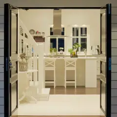 Välkomnande groventré inspiration: Öppna dörrar visar ett ljust kök med köksö och trappa. Utanför syns en stol och en olivträd.