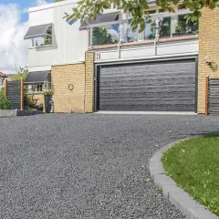 En vacker uppfart med mörkt grus som leder fram till ett modernt hus med garageport.