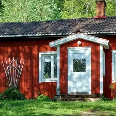 Röd stuga med vita knutar och tegeltak, omgiven av grönska. En klassisk bild som visar skillnad på torp och stuga.