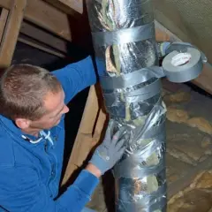 Man tejpar isolerad ventilationskanal i en friggebod.