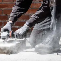 Person slipar betong med vinkelslip. Damm virvlar upp runt arbetsområdet.
