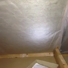 Insidan av en vind som ska tömmas. Synliga träreglar och isolering under plast.