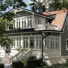 Vackert putsade hus med gröna träfasader och vita detaljer. En veranda med vita möbler och en uteplats inbjuder till avkoppling. Perfekt inspiration för putsade hus.