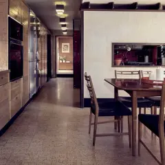 Kök och matplats i ett funkishus från 60-talet. Lång köksbänk med trädetaljer och rostfria vitvaror. Runt matbord med stolar.