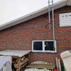Röd tegelfasad konstruktion med ett fönster och en vit garageport. Vedhögar och möbler syns framför huset.