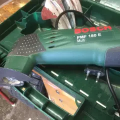 Bosch PMF 180 E multiverktyg med sågblad redo att kapa plasttak. Tillbehör och laddare ligger i lådan.