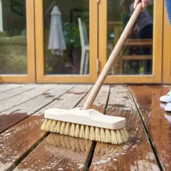 En person använder en borste för att såpa till trallen. Vatten och skum syns på träet.
