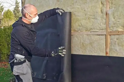 Man med mask rullar ut vindpapp på insidan av en isolerad vägg.