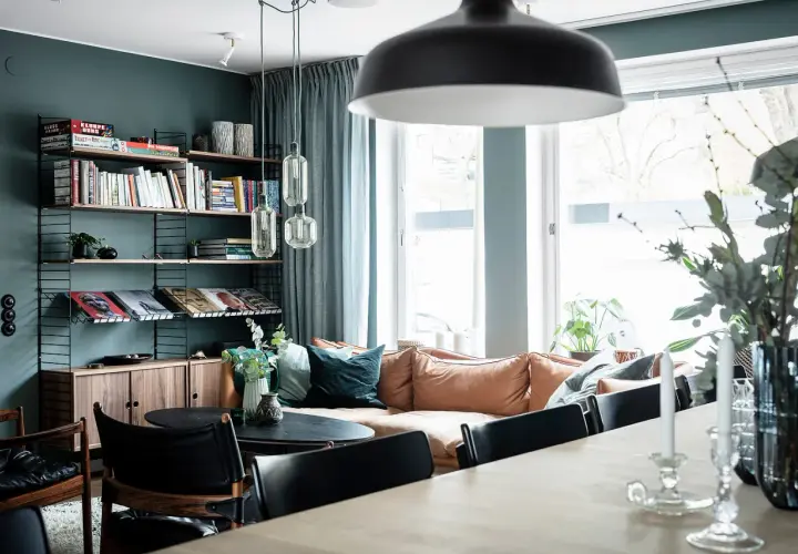 Mysigt vardagsrum med en soffa i mockaimitation, bokhylla och en matplats. En känsla av ett renoverat hus från 50-talet.
