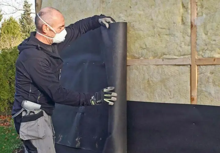 Man med mask rullar ut vindpapp på insidan av en isolerad vägg.