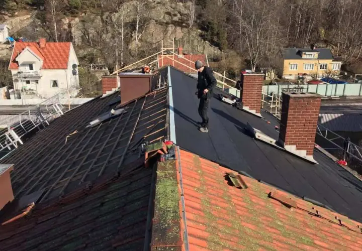 Takläggare arbetar på ett tak där gamla tegelpannor byts ut mot nytt material. Kanske funderar de på aluzink nackdelar inför framtida projekt.