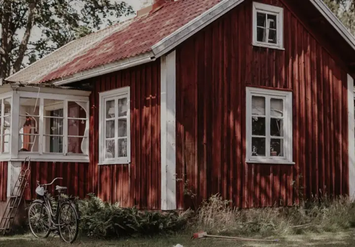 Rött torp med glasveranda, en cykel och en stege står på gräsmattan.