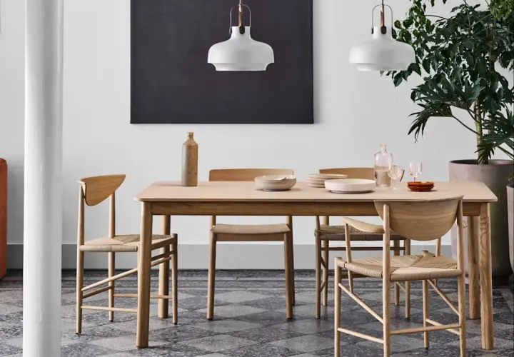 Ett ljust träbord med stolar i naturmaterial, en vas och tallrikar. Lamporna ovanför och den stora gröna växten bidrar till en känsla av antroposofisk inredning.