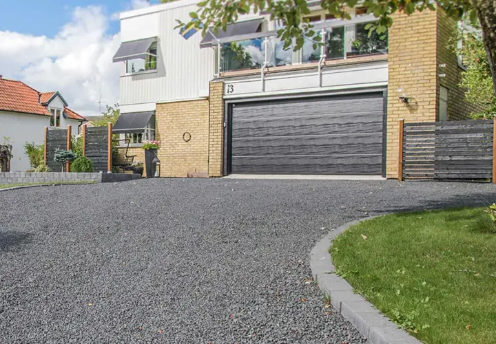 En vacker uppfart med mörkt grus som leder fram till ett modernt hus med garageport.