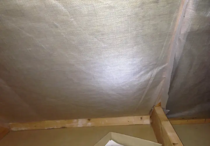 Insidan av en vind som ska tömmas. Synliga träreglar och isolering under plast.