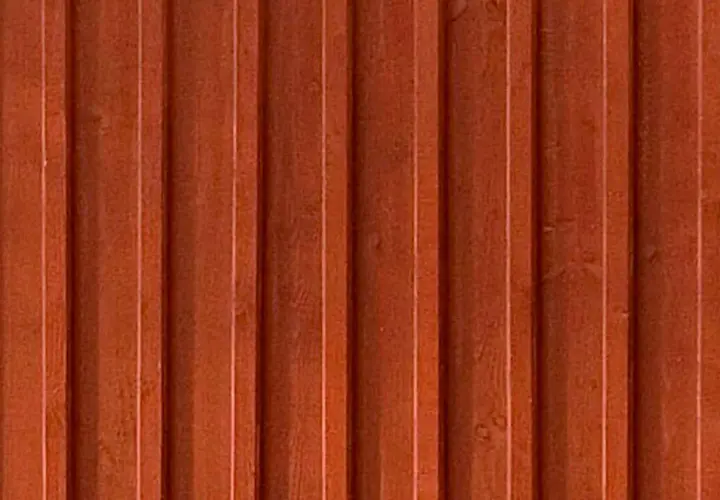 En vägg av gammaldags lockpanel i faluröd färg. Träets ådring syns svagt under färgen.
