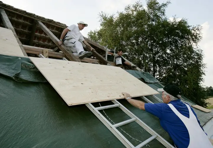 Takläggare arbetar på ett tak med råspont vilken sida upp. En stor plywoodskiva placeras på plats.