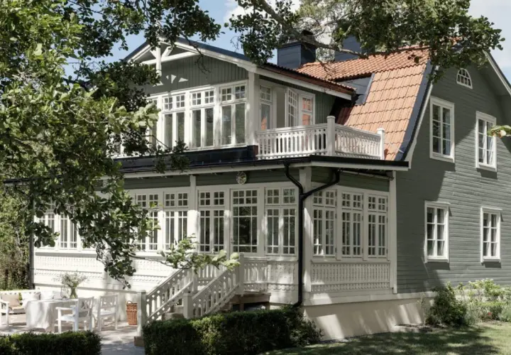 Vackert putsade hus med gröna träfasader och vita detaljer. En veranda med vita möbler och en uteplats inbjuder till avkoppling. Perfekt inspiration för putsade hus.