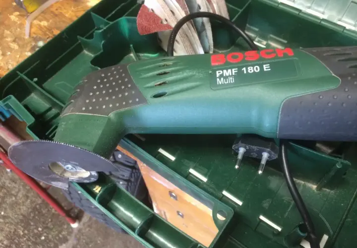 Bosch PMF 180 E multiverktyg med sågblad redo att kapa plasttak. Tillbehör och laddare ligger i lådan.