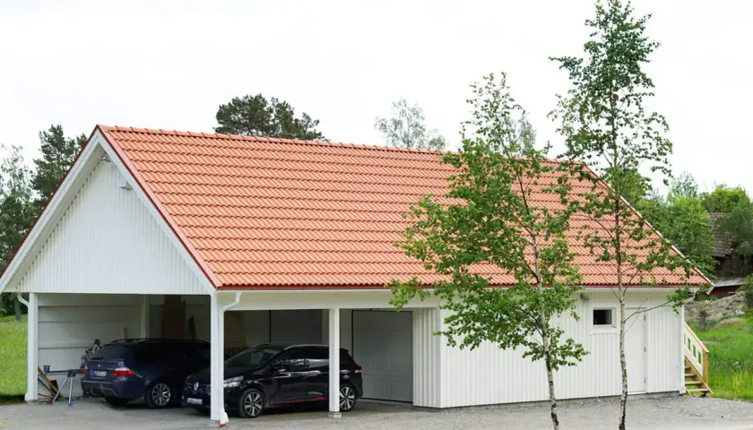 Ett vitt hus med tegeltak, där en del är en carport med två bilar och en annan del är ett garage. Kanske en ombyggnad för att bygga om carport till garage.