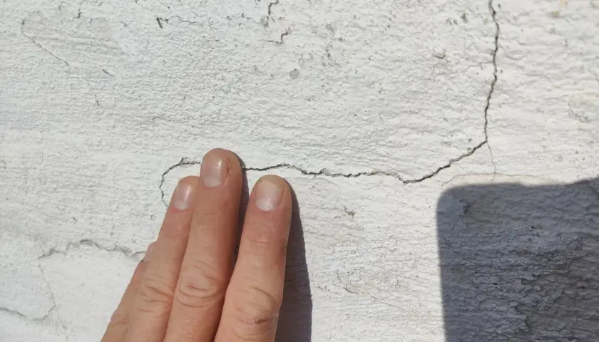 En hand pekar på en spricka i en vit tegelfasad.