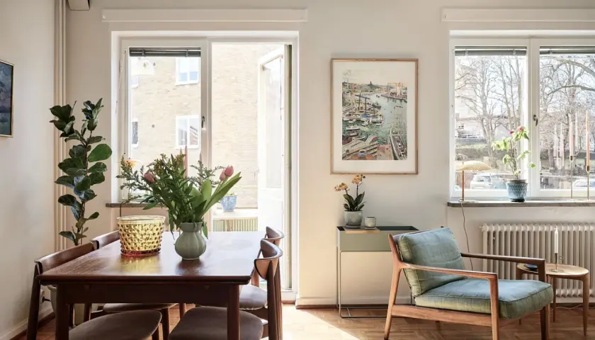 Vardagsrum med matplats i ett 20-tals hus arkitektur. Solstrålar lyser upp trägolvet och möblerna.