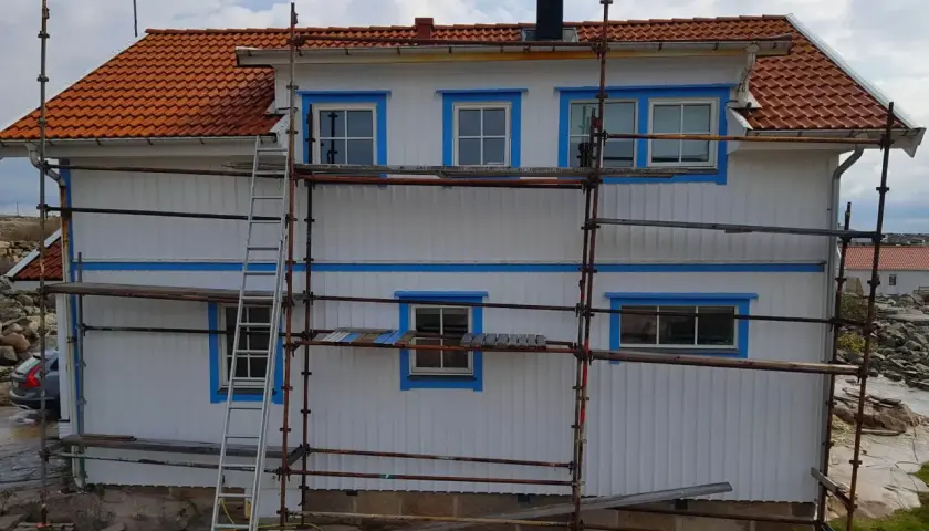 Ställningar runt ett vitt hus med orange tak. Arbetet med att isolera gammalt hus utifrån pågår.
