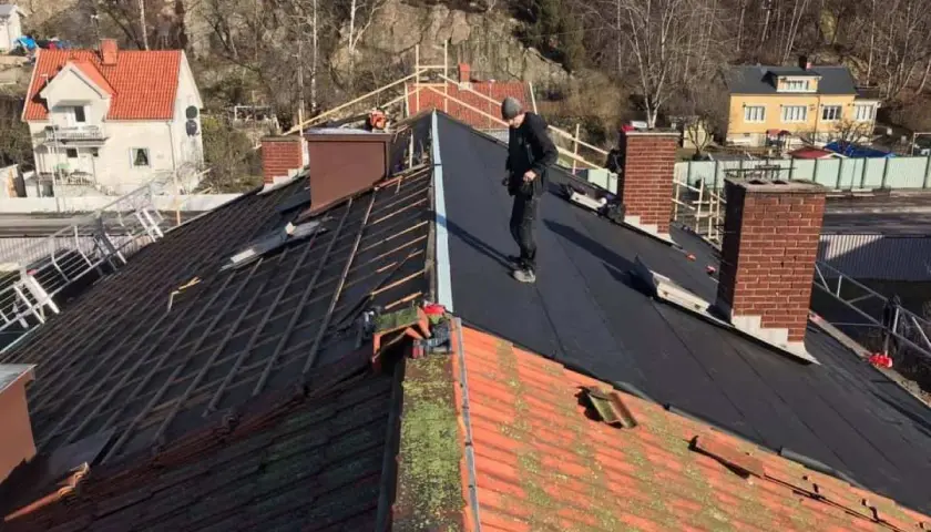 Takläggare arbetar på ett tak där gamla tegelpannor byts ut mot nytt material. Kanske funderar de på aluzink nackdelar inför framtida projekt.