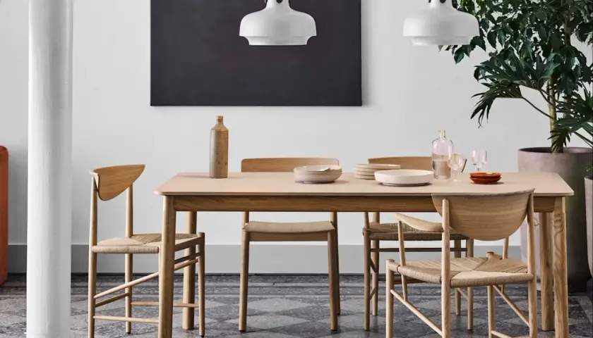 Ett ljust träbord med stolar i naturmaterial, en vas och tallrikar. Lamporna ovanför och den stora gröna växten bidrar till en känsla av antroposofisk inredning.