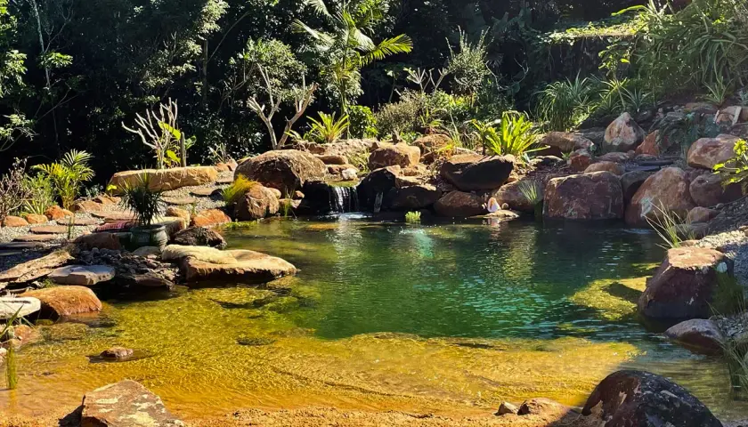 En person sitter vid en vacker natur pool omgiven av stenar och frodig grönska.