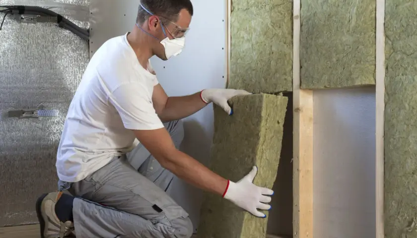 Man med skyddsutrustning installerar tjock isolering i taket.