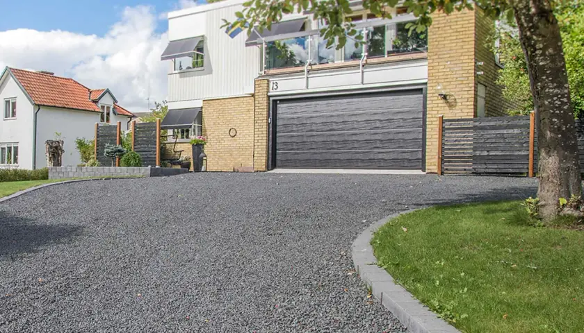 En vacker uppfart med mörkt grus som leder fram till ett modernt hus med garageport.
