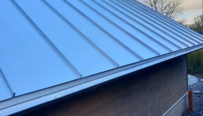 Ett modernt enkelfalsat plåttak på en träfasadbyggnad. Taket är silverfärgat och har en ren, stilren design.
