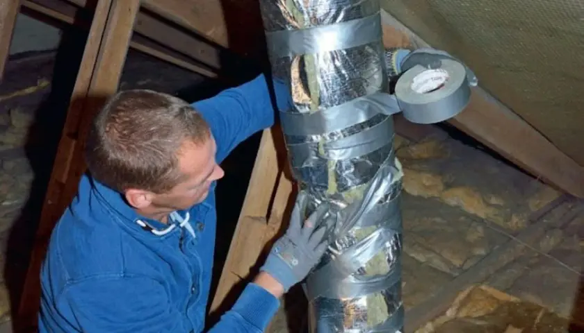 Man tejpar isolerad ventilationskanal i en friggebod.
