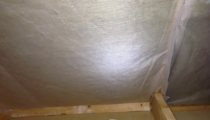 Insidan av en vind som ska tömmas. Synliga träreglar och isolering under plast.